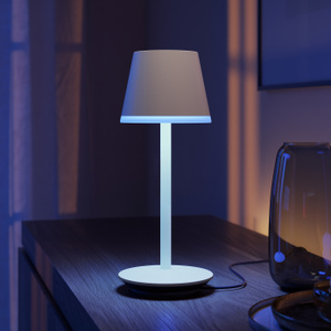 The Philips Hue Go Portable Table Lamp on a table top in a darkened room.