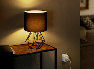 The Eve Energy plug, inserted into a standard power socket with green LED power indicator ON, connected to a lamp.