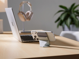 Moft MagSafe Wallet-standaard, achterkant, iPhone in liggende oriëntatie, bevestigd aan wallet-standaard in staande oriëntatie, geplaatst op een bureau naast een MacBook