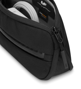 Split Kit de Aer, parte superior, color negro, compartimento con la cremallera abierta en la parte superior, cargador USB-C y cable insertado en los bolsillos interiores, etiqueta con el logo de Aer cosida en el interior