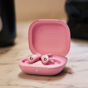 Powerbeats Fit-oortjes in de kleur krachtig roze, in een oplaadcase in dezelfde kleur naast sportspullen, om te laten zien hoe draagbaar ze zijn. 