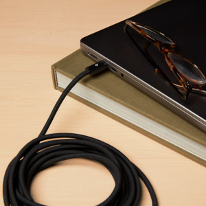 Beats USB-C to USB-C Woven Cable in Bolt Black plugged into MacBook Pro, coiled up to show 3 m / 10 ft length. 
