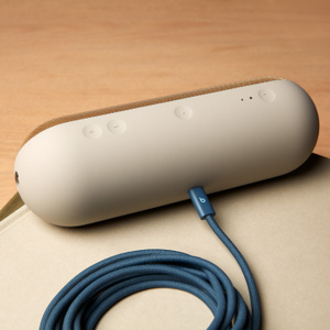Cáp Bện USB-C sang USB-C của Beats màu Xanh Đêm gắn vào loa Beats Pill màu Vàng Champagne, được cuộn lại để cho thấy độ dài 3 m. 