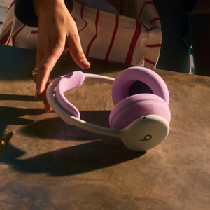 핑크 색상 헤드밴드 쿠션과 이어컵 쿠션이 장착된 클라우드 색상 Beats 360을 향해 손을 뻗는 사람