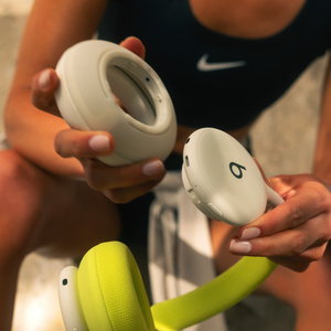 شخص يحمل سماعات Beats 360 بلون أبيض الغيوم مع بطانة الإطار المحيط بالرأس وغطاء الأذنين بلون فولت نيون وأبيض الغيوم