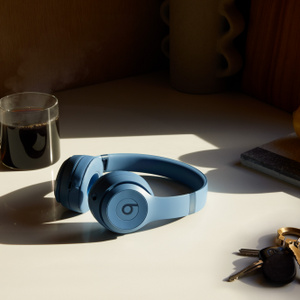 Beats Solo 4 kabellose Kopfhörer in Schieferblau liegen neben Büchern auf einem Tisch.