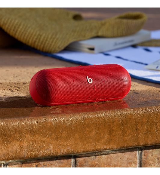 Haut-parleur Bluetooth® Beats Pill en rouge relevé à l’extérieur.
