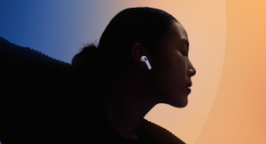 AirPods 5, white colour, worn in the ear, person silhouetted against multicoloured background