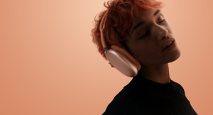 Eine Person trägt AirPods Max 2, Farbe: Orange, Kopf geneigt, Augen geschlossen, orangener Hintergrund