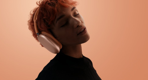 سيدة تضع على رأسها سماعات AirPods Max 2، بلون برتقالي، رأسها مائل، عيناها مغمضتان، خلفية برتقالية