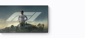 Apple TV promo, title: F1 the Movie, Brad Pitt wearing Formula One racing attire, looking to the side confidently and stoically, set in front of a F1 racing car against a background of tyre smoke and dark blue sky