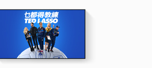 Apple TV 4k 顯示 Apple TV 的宣傳圖，片名為《乜都得教練》(Ted Lasso)，演員們於藍色漸變背景前，在巨型足球上呈扇形排開，Jason Sudeikis 笑容滿面，Juno Temple 微笑並叉腰，Brett Goldstein 身穿皮革外套，Hannah Waddingham 舉起拳頭，Brendan Hunt 拿著寫字板。
