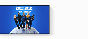 Apple TV 4K에 표시되어 있는 제목이 ‘테드 래소’인 Apple TV 프로모션 이미지. 환하게 미소 짓는 제이슨 서디키스, 한 손을 허리에 얹고 미소 짓는 주노 템플, 가죽 재킷을 입은 브렛 골드스타인, 주먹을 들어 올린 한나 웨딩햄, 클립보드를 들고 있는 브렌든 헌트 등의 출연진이 커다란 축구공 위에 부채꼴로 서있으며, 배경은 파란색 그라데이션입니다.