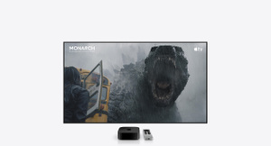 Apple TV 4K, color negro, y mando Siri Remote, color plata, colocado debajo de una gran pantalla de televisión