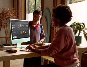A person works on iMac at their desk, typing on Magic Keyboard, while talking to a child on the other side of the desk 
