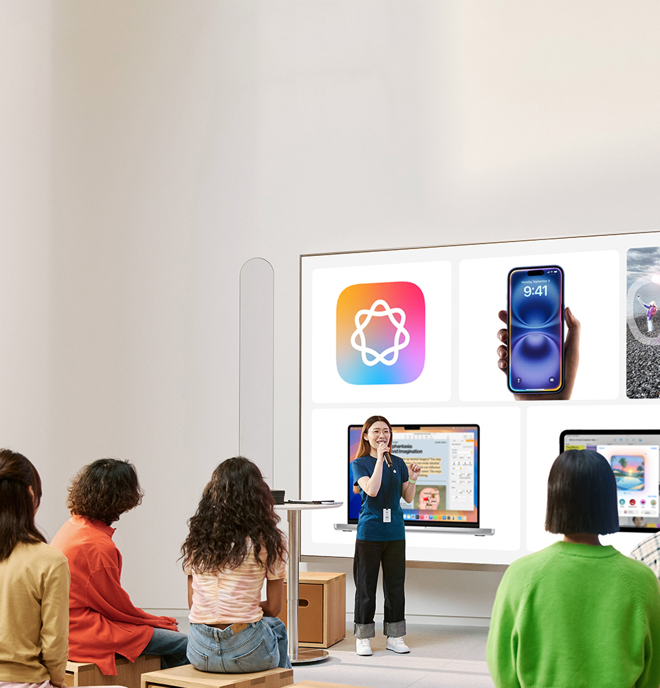 People sit on cubes facing an Apple Creative and a Video Wall displaying the Apple Intelligence logo, iPhone, Mac, and iPad.