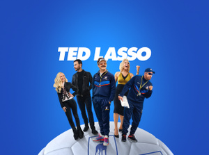 Apple TV+ promo, title: Ted Lasso, Jason Sudeikis smiling broadly, Juno Temple smiling with her hand on her hip, Brett Goldstein in a leather jacket, Hannah Waddingham with fist raised, Brendan Hunt holding a clipboard, cast fanned out on an oversized soccer ball, blue gradient background.