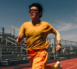 A person wearing an Apple Watch runs on a track outside under a clear blue sky