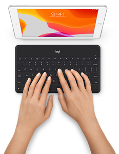 Las manos de una persona escribiendo en el teclado muestran la fila completa de teclas de atajos para iOS y la amplia distribución de unas teclas suaves y silenciosas.