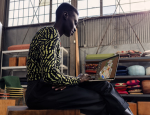 Une personne assise utilise un MacBook Air posé sur ses genoux. 