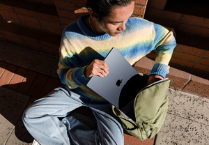 Une personne assise par terre glisse un MacBook Air 15 pouces dans son sac à dos.