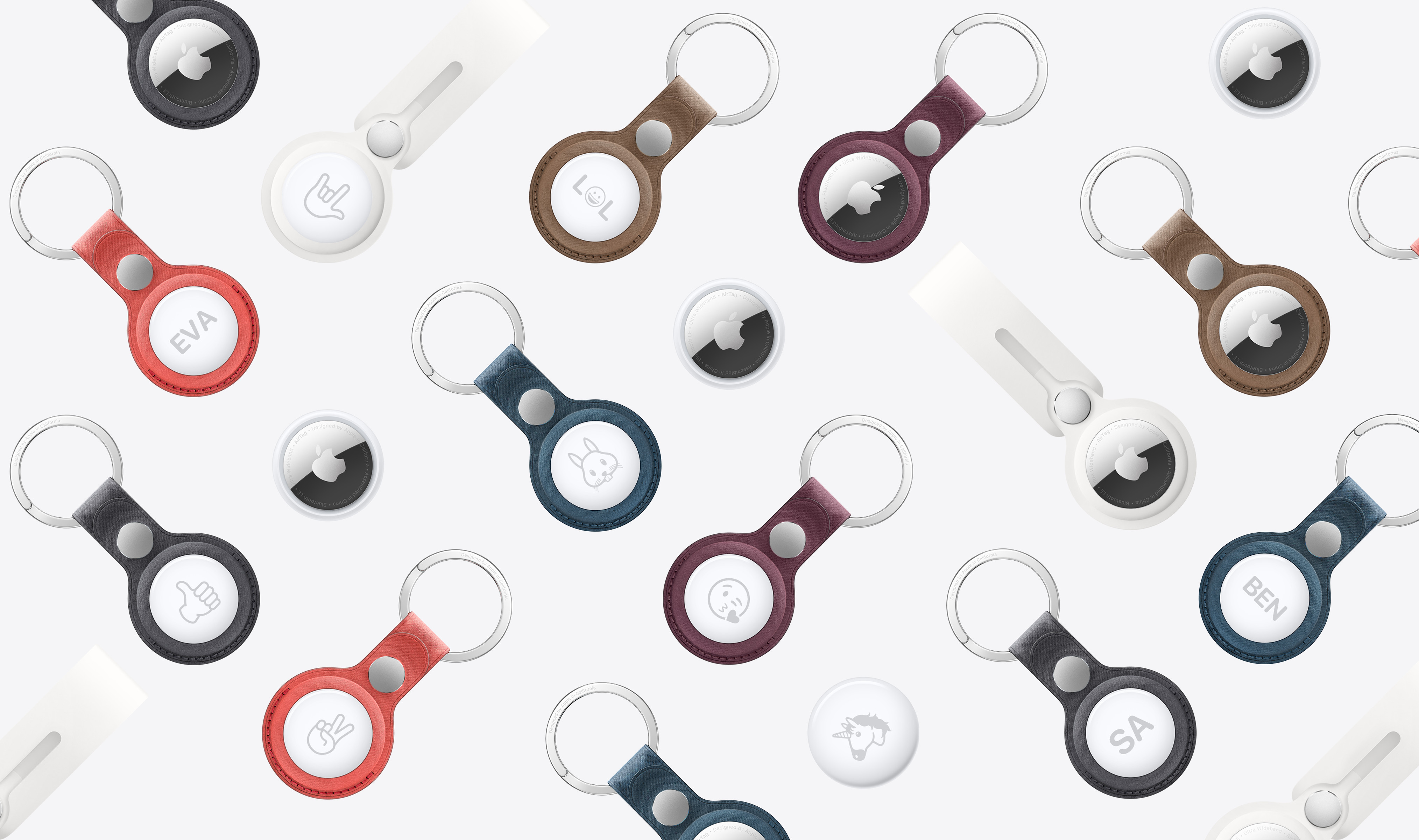 Top view of several AirTag, some in colored keychains and loops. Some AirTag show the Apple logo while others show emoji or letter engravings.