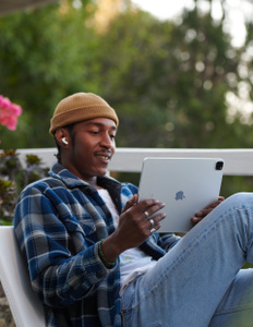 Person sitting outdoors, looking at an iPad, listening to AirPods